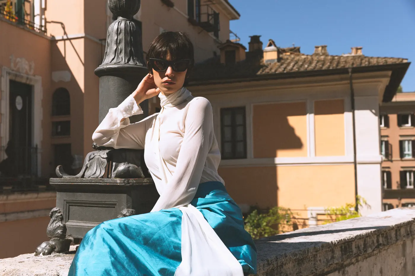 A model sitting on a terrace parapet, rooftops behind her