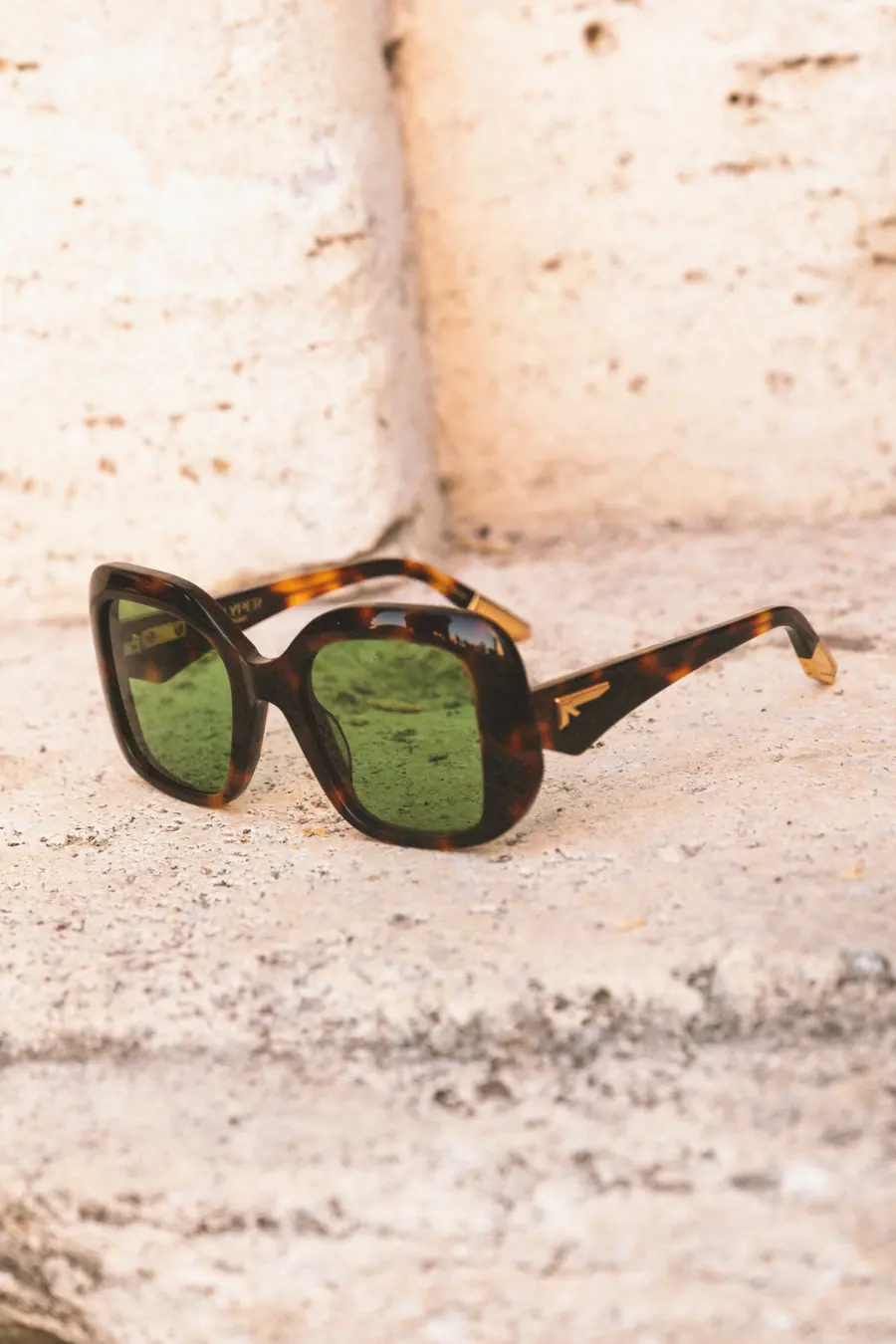A tortoiseshell frame with green lenses in the sun on stone