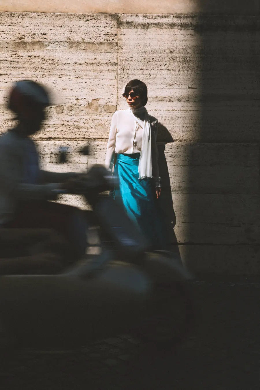 A model against a wall, a scooter blurring past